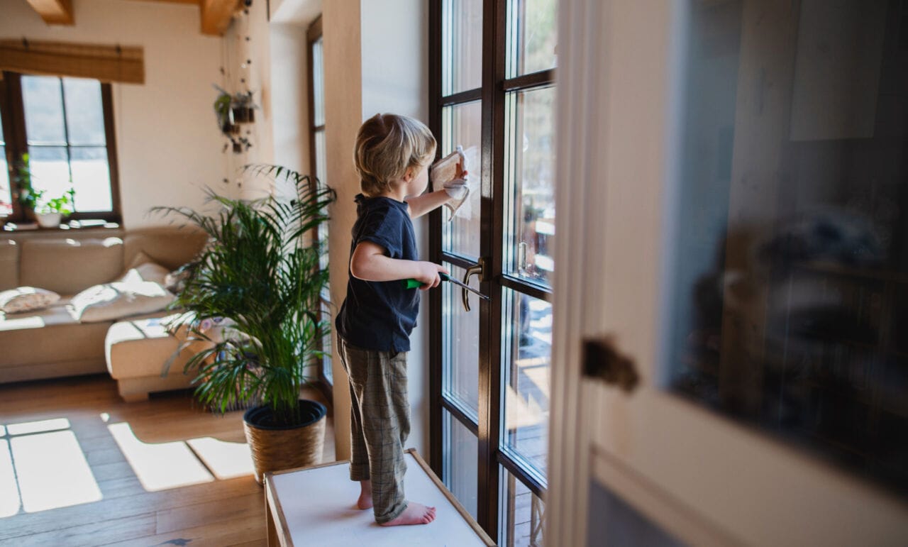 Side view of little boy cleaning windows indoors at home, daily chores concept.