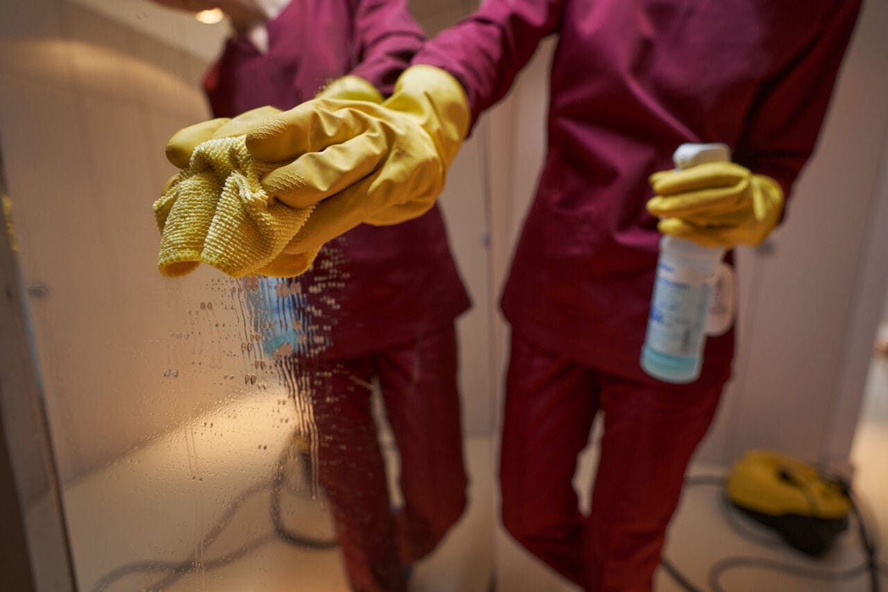 Professional janitor cleaning mirror in apartment hall